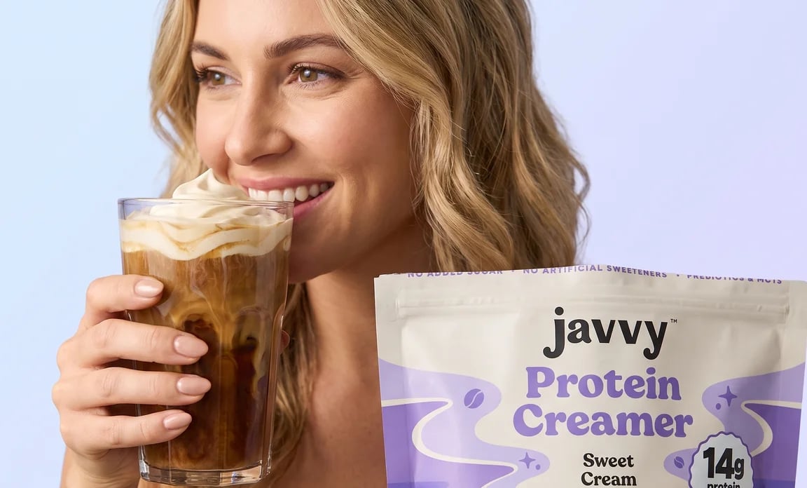 Woman sipping an iced coffee next to a bag of Javvy Protein Creamer