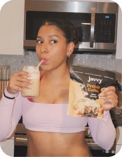 Customer sipping an iced Javvy Protein Coffee in her kitchen