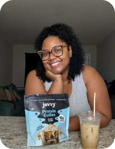 Customer smiling next to a bag of Javvy Protein Coffee and an iced coffee