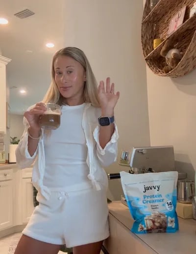Customer waving in her kitchen with a Javvy Protein Creamer bag on the counter