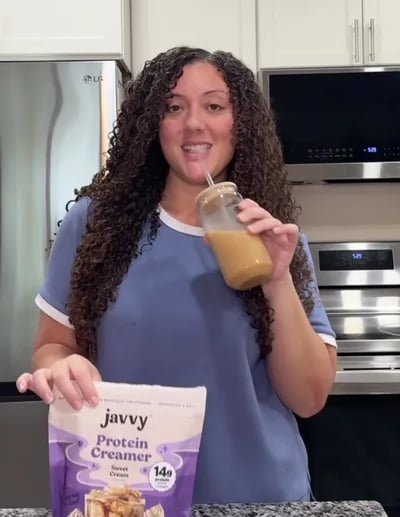 Customer in her kitchen with an iced coffee and a bag of Javvy Protein Creamer
