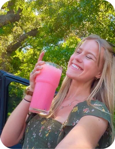 Customer outdoors sipping a pink Protein Refresher from a tumbler