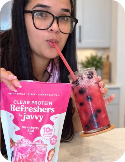 Customer sipping a pink Protein Refresher next to a bag of Javvy Protein Refreshers