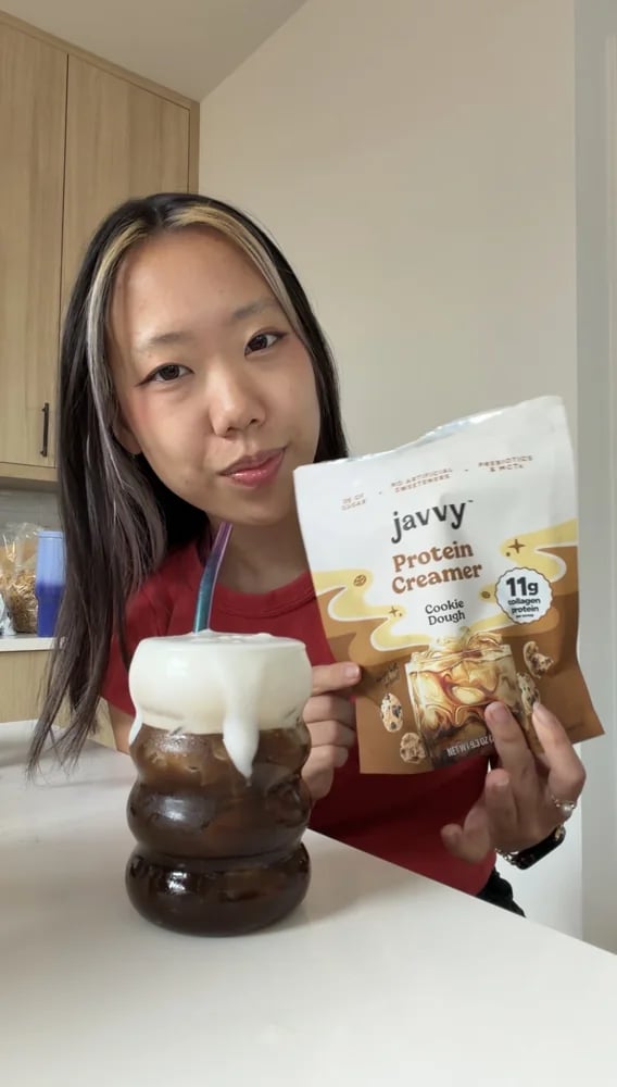 Customer holding a bag of Javvy Protein Creamer next to an iced coffee