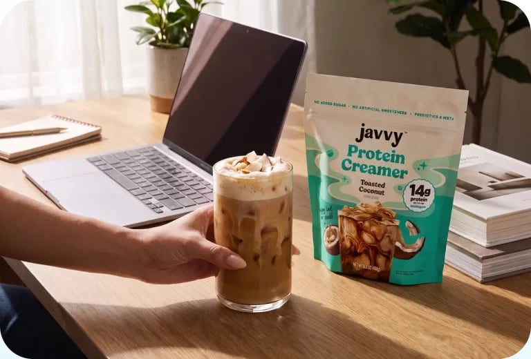 Iced coffee and a bag of Protein Creamer on a desk next to a laptop