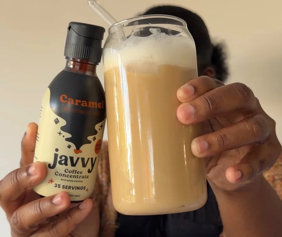 Customer holding a bottle of Caramel Coffee Concentrate next to an iced latte